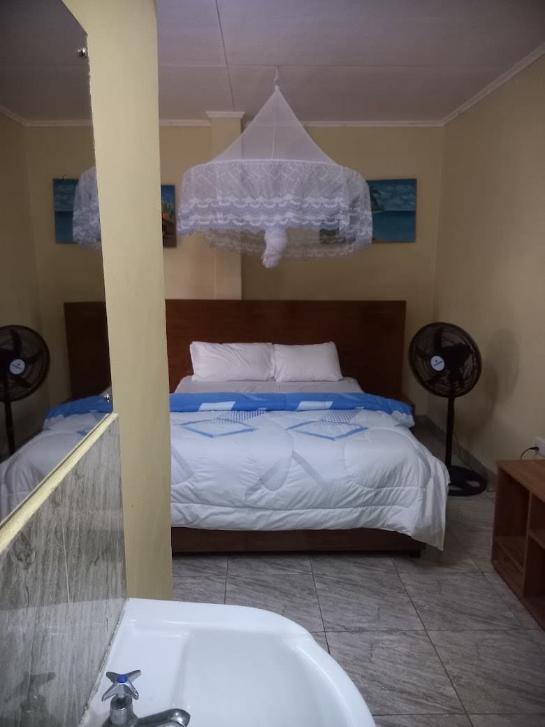 Guest room with a double bed and a white duvet, seen past the wash basin inside the room