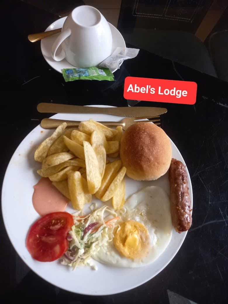 Breakfast with a fried egg, chips, a sausage, a bread roll, coleslaw, tomato and a cup of tea