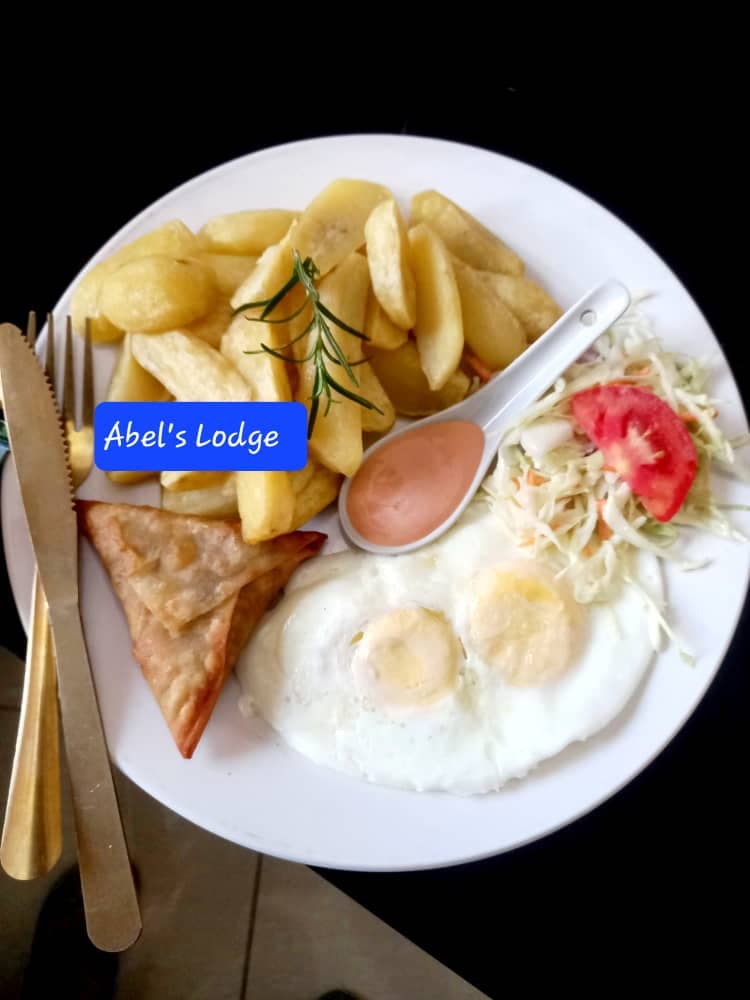 Breakfast plate with fried eggs, potato wedges with rosemary, a samosa, coleslaw and tomato